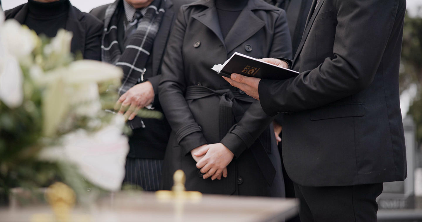 Bible, hands and family at funeral, cemetery or burial ceremony